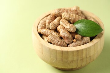 Tumeric rhizomes with leaf in bowl on light green background, closeup. Space for text