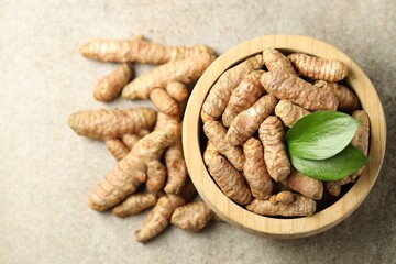 Tumeric rhizomes with leaves in bowl on grey table, top view