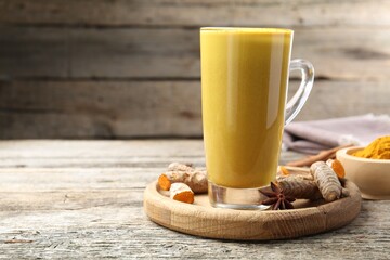 Delicious turmeric latte in glass cup, roots and spices on wooden table, closeup. Space for text