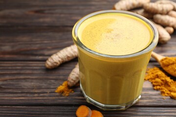 Delicious turmeric latte in glass, roots and powder on wooden table, closeup