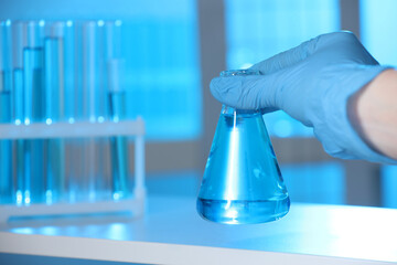 Woman holding flask with blue liquid indoors, closeup