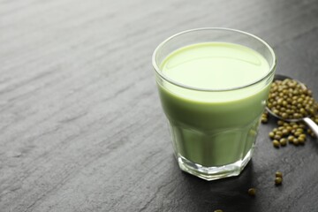 Fresh mung bean juice in glass and seeds on black table, closeup. Space for text