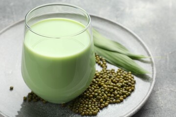 Fresh mung bean juice in glass, seeds and green leaves on grey table, closeup