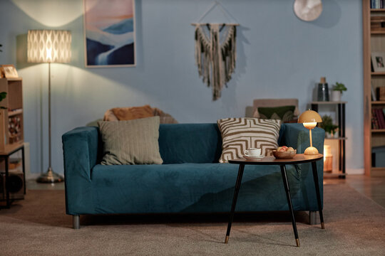 Interior of minimalist living room with blue sofa, coffee table and lamps filling room with low key light, copy space