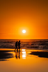 Golden Sunrise walk along Northeast beach couple silhouette with reflections 