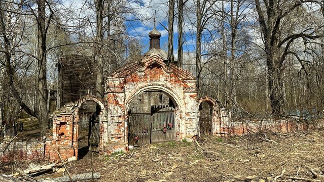 Dilapidated old building with a brick archway and a small window. An abandoned ancient Russian cemetery in the woods with a wooden church.