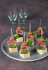 Canape with sausage, cucumber, cheese and olives on gray plate