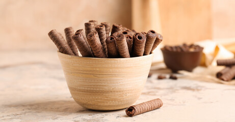 Bowl with delicious chocolate wafer rolls on beige table