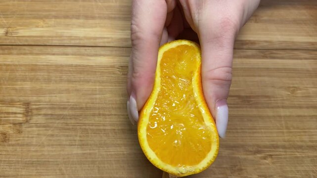 Close up of hands squeezing orange for juice. Human using their hands to squeeze half citrus to make the orange juice into the glass. Making orange juice pressing half of orange.
