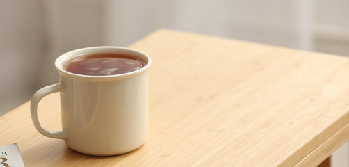 Mug of hot black tea on wooden table in room. Banner for design