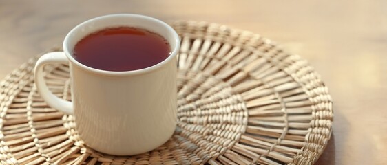White mug of hot black tea on wicker mat