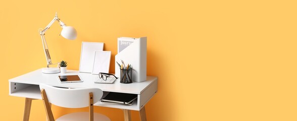 Comfortable workplace with tablet computer, lamp and supplies near orange wall. Banner for design