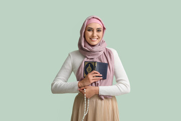 Fototapeta premium Young Muslim woman with Koran and prayer beads on green background. Islamic New Year celebration
