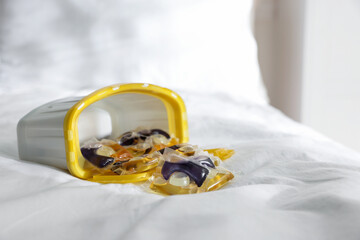Laundry detergent capsules in container on white fabric, closeup. Space for text