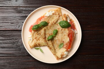 Delicious crepes with salmon, cream cheese and basil on wooden table, top view