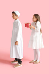 Little girl greeting Muslim boy with gift on pink background