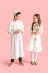 Little Muslim children with praying beads and Arabic lamps on pink background