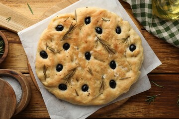 Delicious focaccia bread with olives, rosemary and salt on wooden table, flat lay