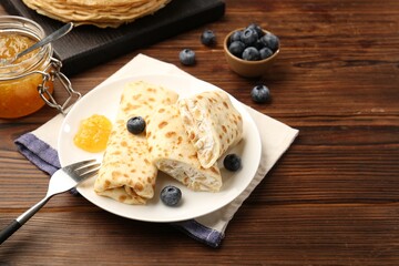 Delicious crepes with cottage cheese, jam and blueberries served on wooden table