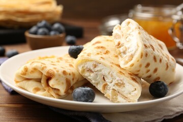 Delicious crepes with cottage cheese, jam and blueberries on wooden table, closeup