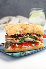 Delicious baguette sandwich with caviar, ham and capers on white wooden table