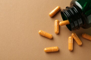 Turmeric capsules and overturned bottle on beige background, flat lay. Space for text