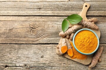 Turmeric powder in bowl, roots and leaves on wooden table, flat lay. Space for text