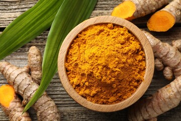 Turmeric powder in bowl, roots and leaves on wooden table, flat lay