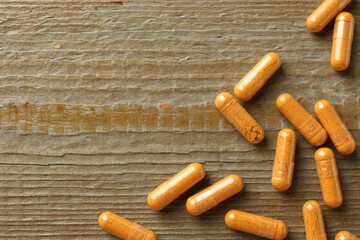 Turmeric capsules on wooden table, flat lay. Space for text