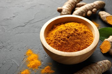 Aromatic turmeric powder in bowl and fresh roots on black table, closeup. Space for text