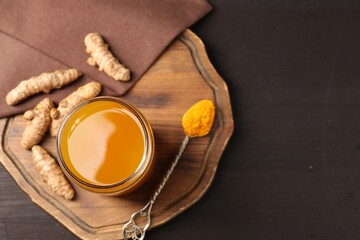 Aromatic turmeric tea in glass, roots and powder on wooden table, top view. Space for text