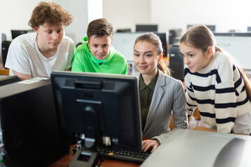 Fototapeta premium Female teacher helping schoolboy and schoolgirl in computer class