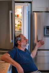 Middle-aged man resting against an open fridge