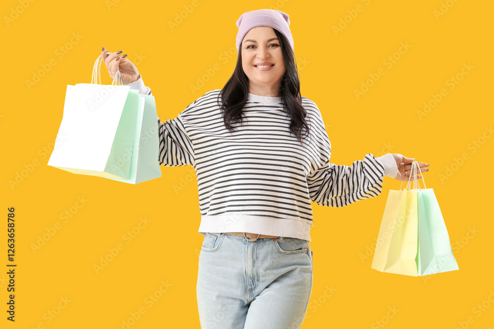 Wall mural Beautiful happy mature woman with shopping bags on yellow background. International Women's Day