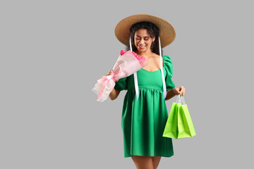 Fashionable African-American woman with bouquet of flowers and shopping bags on grey background. International Women's Day celebration