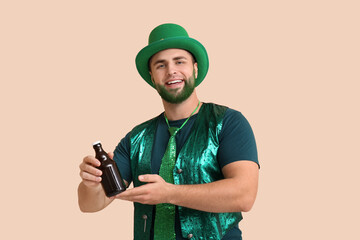 Young man in leprechaun hat with green beard holding bottle of beer on beige background. St....