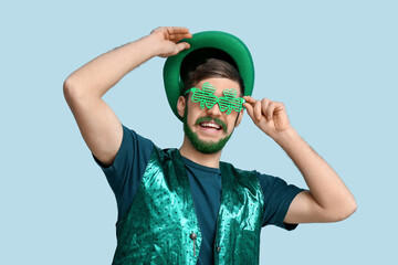 Young man in leprechaun hat and decorative glasses in shape of clover with green beard on blue...