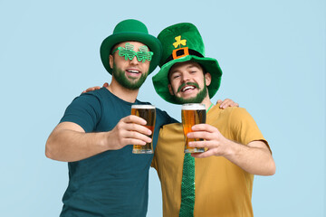 Happy young men in leprechaun hats with green beards holding glasses of beer on blue background....