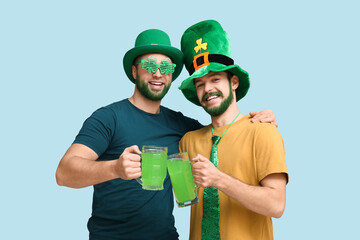 Happy young men in leprechaun hats with green beards holding glasses of beer on blue background....
