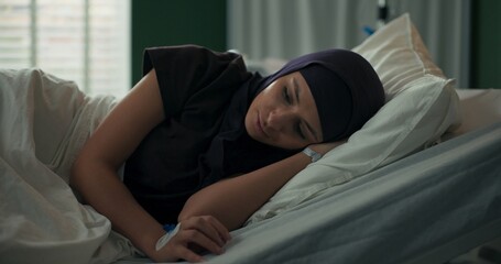 Arab woman rests on her side in hospital room, lost in contemplation.