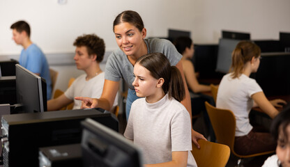 Fototapeta premium Smiling female teenager helping to the female classmate while she is learning computer science in the class