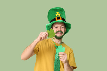 Happy young man in leprechaun hat with green beard holding clover on green background. St....