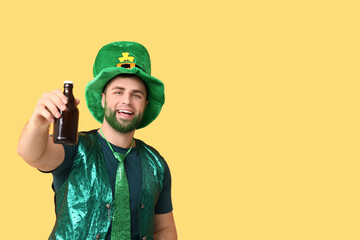 Young man in leprechaun hat with green beard holding bottle of beer on yellow background. St....