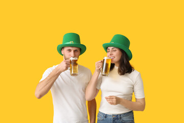 Beautiful young couple in leprechaun hats drinking beer on yellow background. St. Patrick's Day...