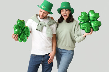 Beautiful young couple in leprechaun hats with air balloons in shape of clover on grey background....