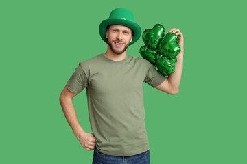 Young man in leprechaun hat with air balloon in shape of clover on green background. St. Patrick's...