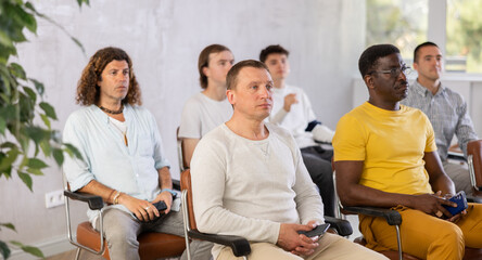 Small group of mature guys attending the lecture with concern sitting on chairs in light room