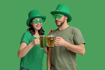 Beautiful young couple in leprechaun hats with glasses of beer on green background. St. Patrick's...