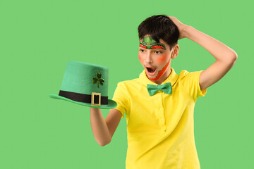 Surprised boy with face painting and leprechaun's hat on green background. St. Patrick's Day...