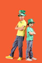 Funny kids with face paintings and leprechaun's hats on orange background. St. Patrick's Day celebration